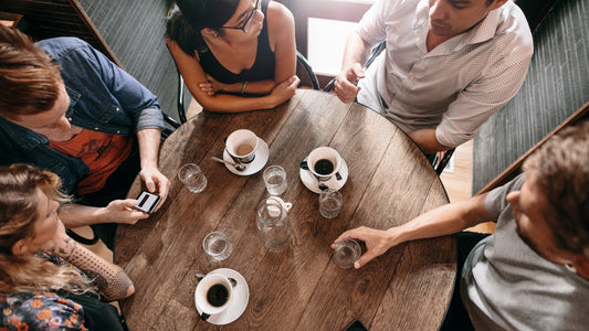 High-angle, bird's-eye view of five people gathered around a rustic round wooden table in a cafe.