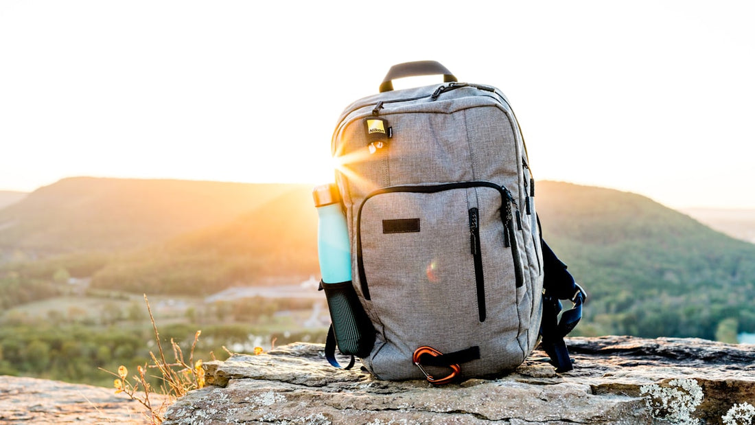 Backpack and water bottle on a rocky outcrop overlooking a green valley at sunset
