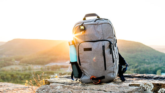 Backpack and water bottle on a rocky outcrop overlooking a green valley at sunset