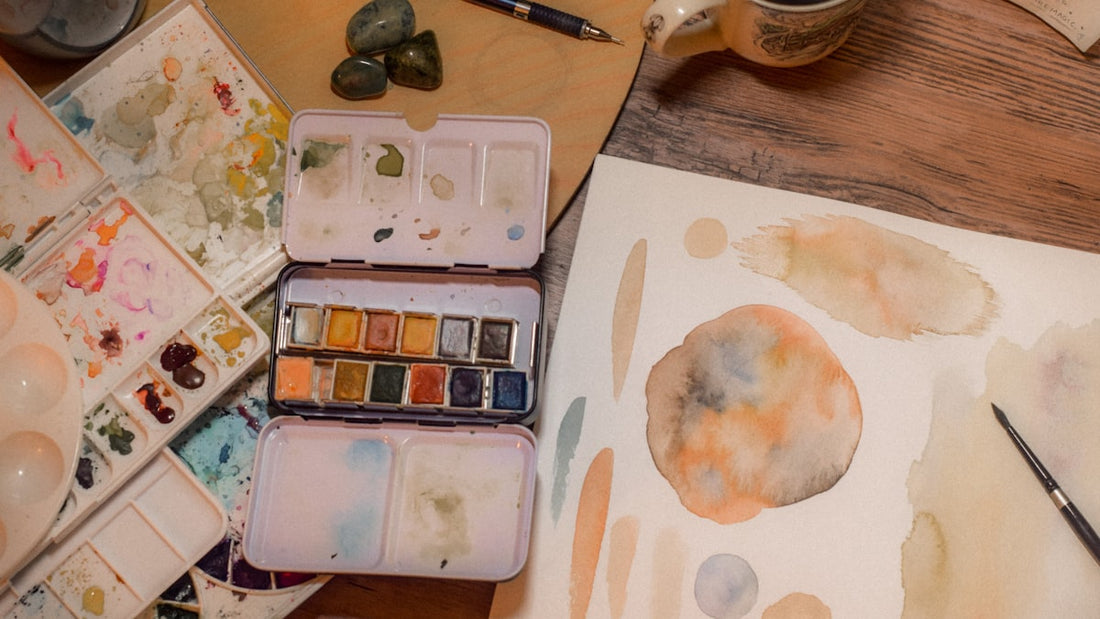 Watercolor palette with paint and a painting in progress on a wooden desk