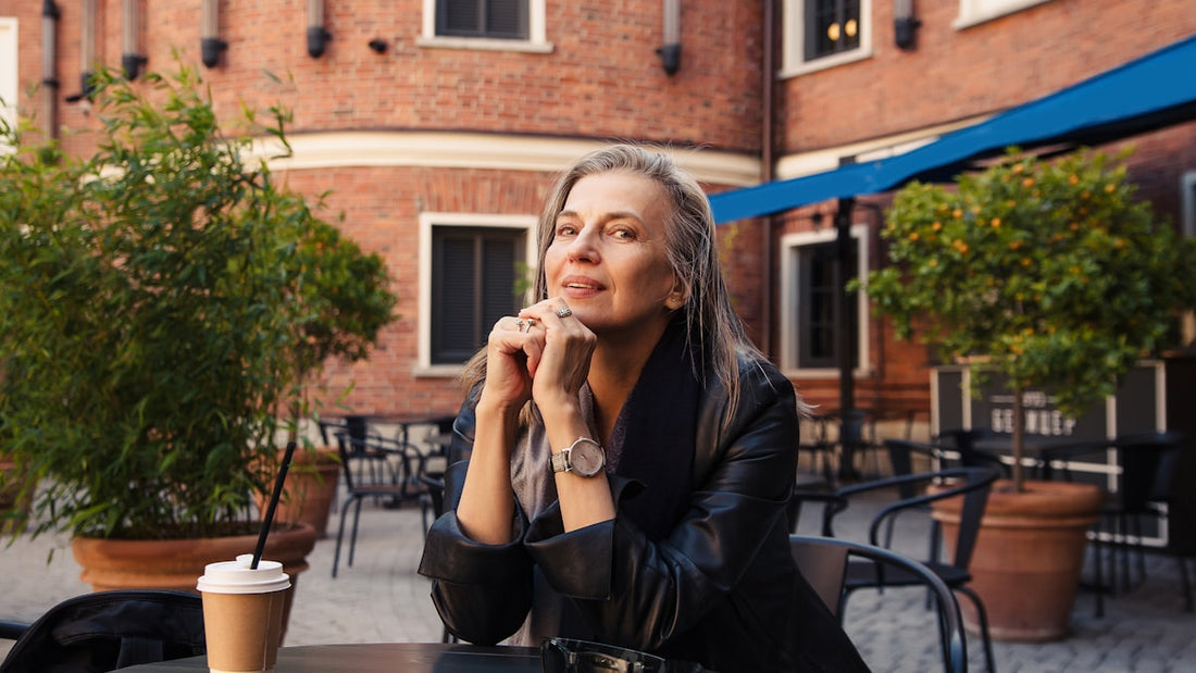 Woman alone at an outdoor cafe table, contemplative, brick building behind her