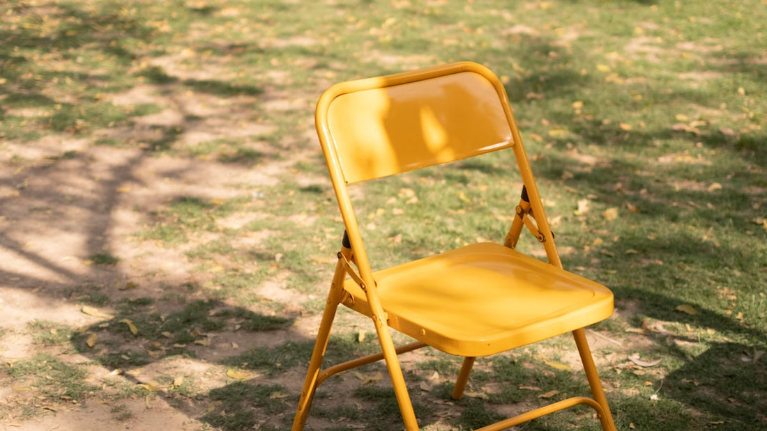 Yellow folding chair sitting alone in dappled sunlight on grass in a quiet park