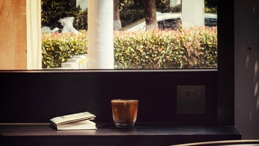 Coffee glass and an open book on a dark windowsill — quiet contemplative scene