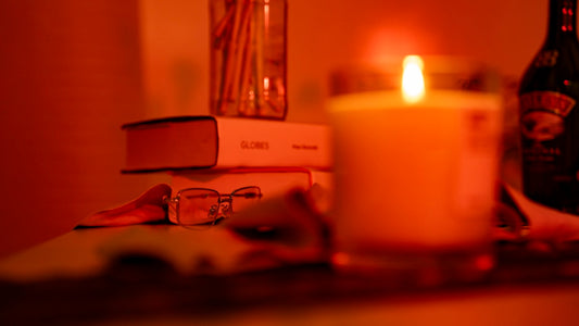 Lit candle on a desk next to stacked books and reading glasses on an open page